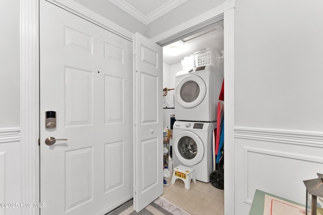 clothes washing area with stacked washer and clothes dryer, wainscoting, crown molding, and a decorative wall