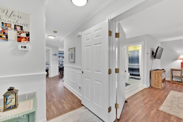 corridor featuring a wainscoted wall, a decorative wall, wood finished floors, and crown molding