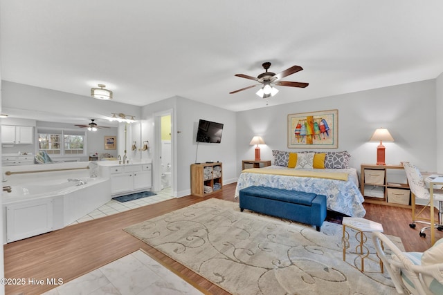 bedroom with a sink, light wood finished floors, ensuite bath, and baseboards