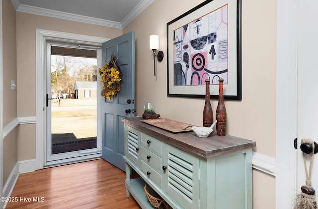 doorway featuring baseboards, crown molding, and light wood finished floors