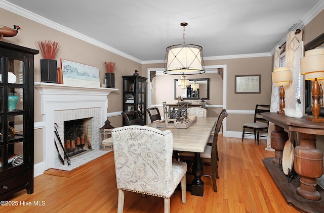 dining room featuring crown molding, light wood-type flooring, a fireplace, and baseboards