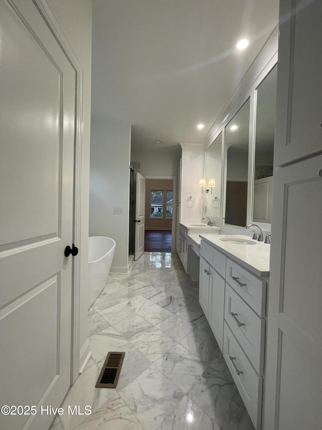 bathroom with marble finish floor, double vanity, a soaking tub, visible vents, and a sink