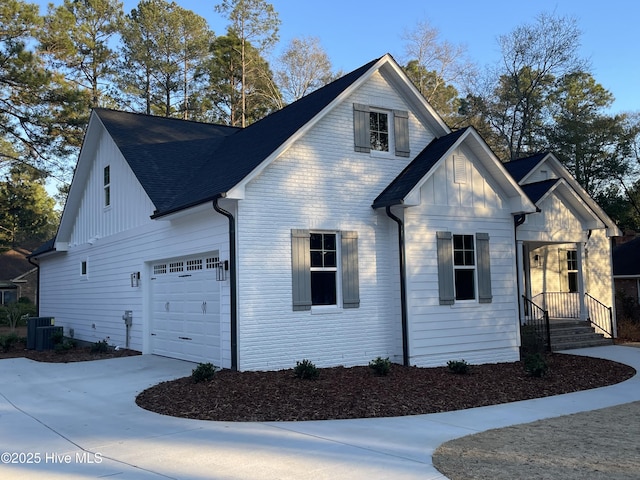 view of front of property featuring board and batten siding, central AC, driveway, and a shingled roof