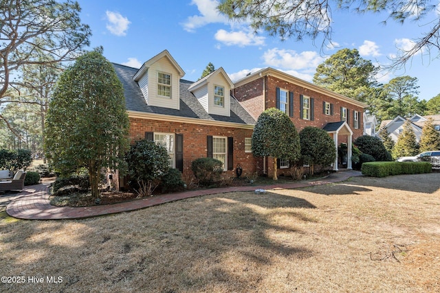 view of front of property featuring roof with shingles, a front yard, and brick siding