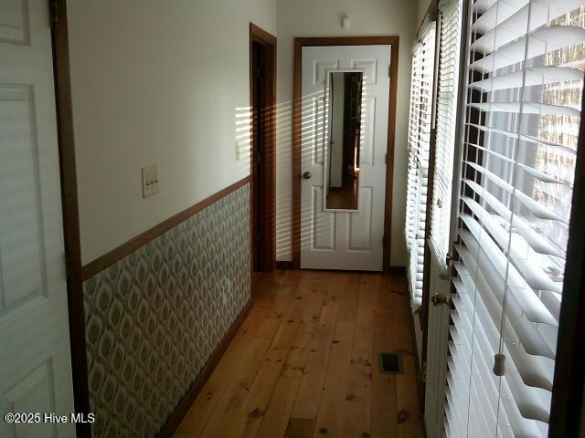 hallway with light wood-type flooring, a wainscoted wall, visible vents, and wallpapered walls