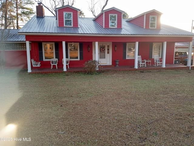 view of front of property with covered porch, metal roof, a chimney, and a front yard