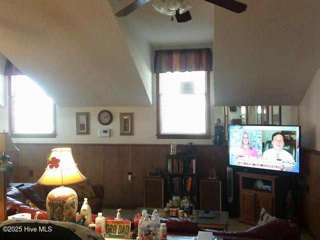 living area with plenty of natural light, ceiling fan, wood walls, and wainscoting