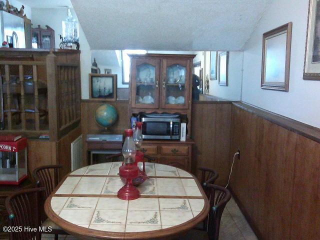 dining area with wood walls, a textured ceiling, and wainscoting