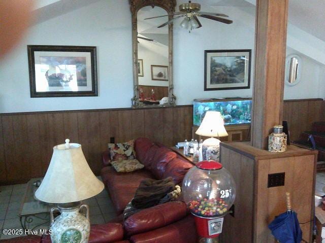 tiled living room featuring lofted ceiling, a wainscoted wall, wooden walls, and a ceiling fan