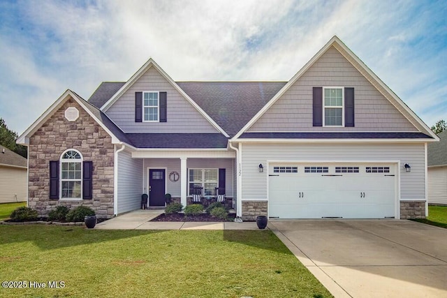 craftsman-style house featuring a shingled roof, concrete driveway, stone siding, covered porch, and a front yard