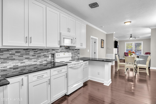 kitchen featuring white appliances, white cabinets, dark countertops, ornamental molding, and a peninsula