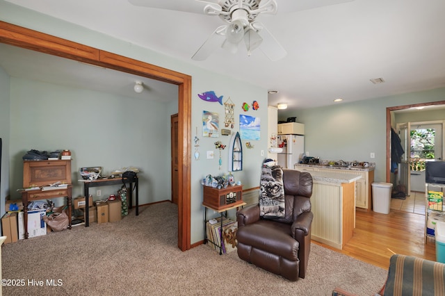 living area with visible vents, light carpet, baseboards, and ceiling fan