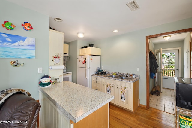 kitchen with white appliances, visible vents, light wood finished floors, a sink, and light countertops