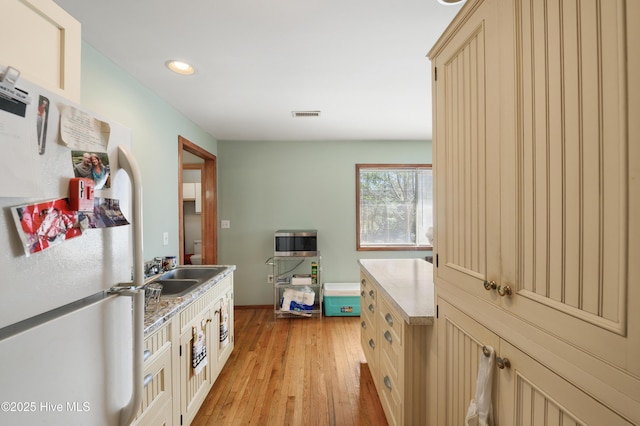 kitchen featuring light wood finished floors, visible vents, freestanding refrigerator, cream cabinetry, and a sink