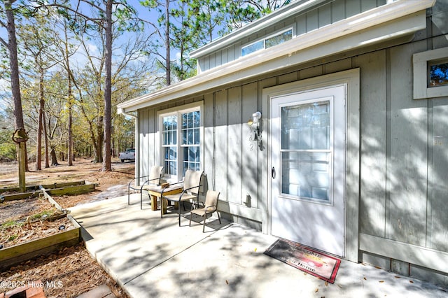 view of exterior entry with board and batten siding and a patio area