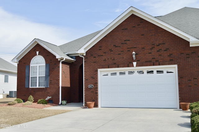 view of front of home featuring brick siding, a shingled roof, central AC unit, a garage, and driveway