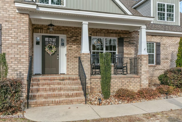 property entrance with a shingled roof, covered porch, and brick siding