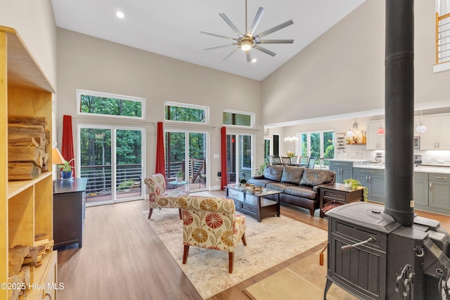 living room with high vaulted ceiling, a ceiling fan, light wood-style floors, a wealth of natural light, and a wood stove