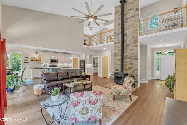 living room featuring visible vents, light wood-style flooring, ceiling fan, a wood stove, and high vaulted ceiling