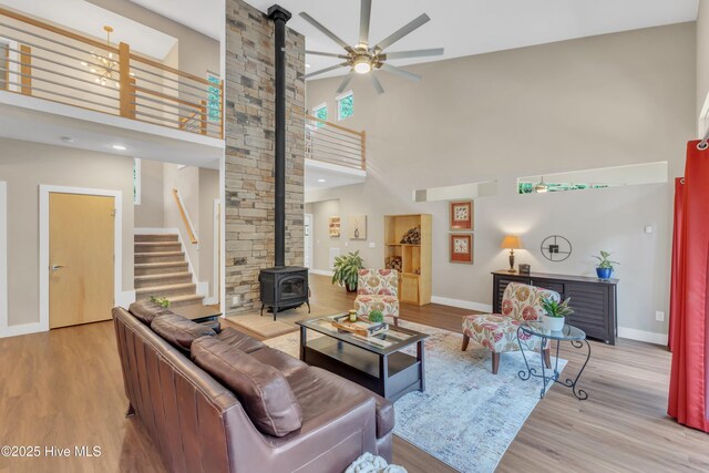 living room with baseboards, a ceiling fan, a wood stove, and light wood-style floors