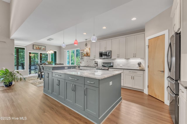 kitchen with decorative light fixtures, a center island with sink, appliances with stainless steel finishes, white cabinets, and light stone countertops