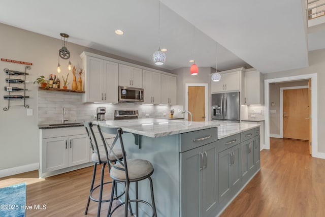 kitchen featuring stainless steel appliances, a sink, white cabinets, hanging light fixtures, and an island with sink