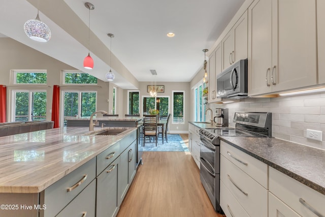 kitchen with stainless steel appliances, a sink, light wood-style floors, tasteful backsplash, and pendant lighting