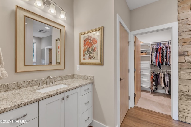 bathroom with vanity, wood finished floors, a walk in closet, and visible vents