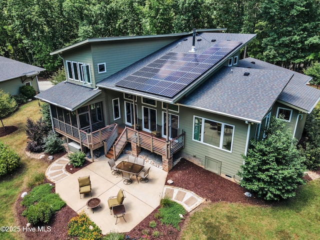 back of house with a shingled roof, an outdoor fire pit, a sunroom, roof mounted solar panels, and stairs