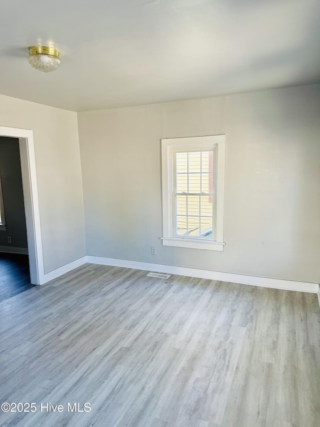 spare room with wood finished floors, visible vents, and baseboards