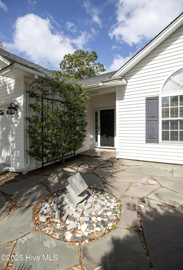 doorway to property featuring a shingled roof and a patio area