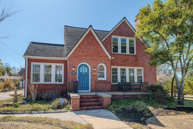 tudor home featuring brick siding and a shingled roof