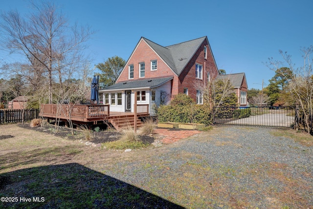 rear view of property featuring a gate, fence, a wooden deck, gravel driveway, and brick siding