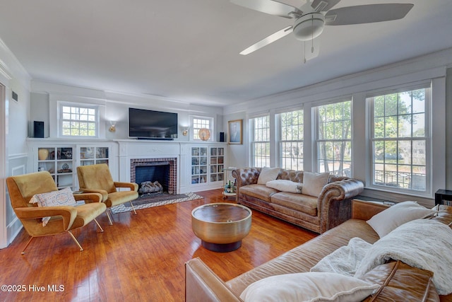 living area with a fireplace, a ceiling fan, wood finished floors, and ornamental molding