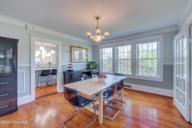 dining area with visible vents, wood finished floors, crown molding, baseboards, and a chandelier