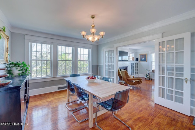 dining room featuring a fireplace, wood finished floors, an inviting chandelier, and ornamental molding