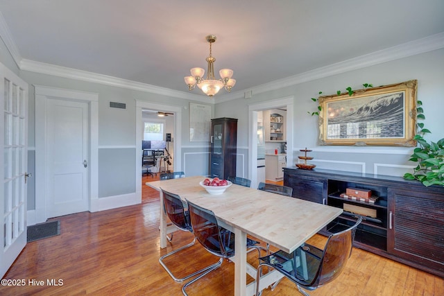 dining room with light wood finished floors, visible vents, a chandelier, and ornamental molding