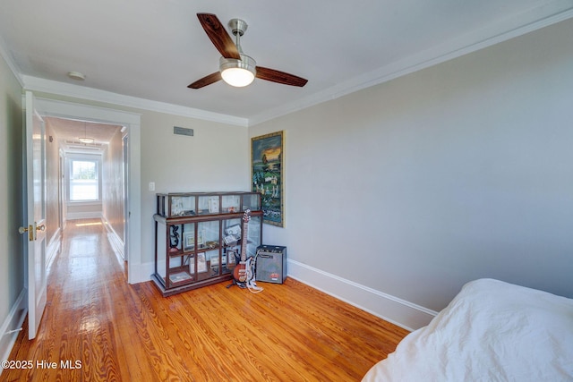 bedroom with crown molding, baseboards, attic access, light wood-style flooring, and a ceiling fan