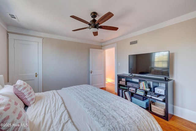 bedroom with baseboards, visible vents, light wood-type flooring, and ornamental molding