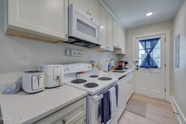 kitchen with white appliances, white cabinets, a sink, and light wood finished floors