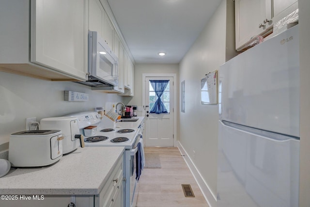 kitchen with visible vents, a sink, light wood-type flooring, white appliances, and baseboards