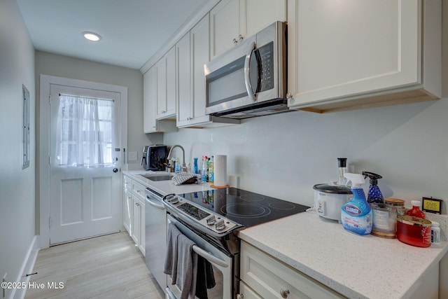 kitchen with light stone counters, light wood finished floors, stainless steel appliances, white cabinets, and a sink