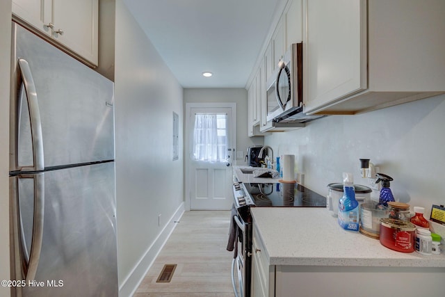 kitchen featuring visible vents, white cabinets, appliances with stainless steel finishes, light wood-style floors, and a sink