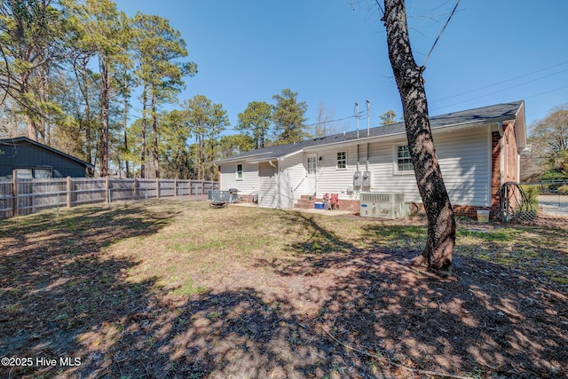 rear view of property with central air condition unit, a fenced backyard, and a yard