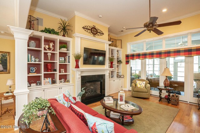 living area with ornate columns, crown molding, and light wood finished floors