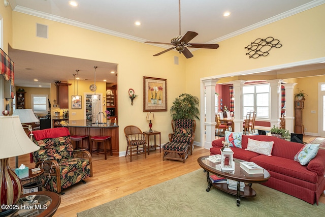 living room with light wood finished floors, visible vents, ornamental molding, a ceiling fan, and ornate columns