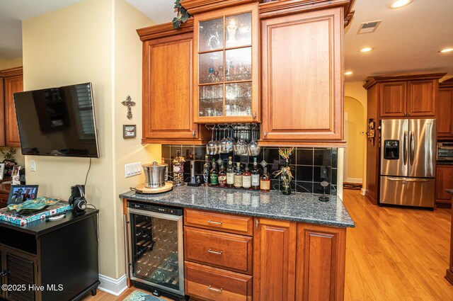 bar with wine cooler, stainless steel refrigerator with ice dispenser, tasteful backsplash, a bar, and light wood-type flooring