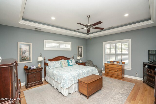 bedroom with visible vents, baseboards, light wood-type flooring, a tray ceiling, and crown molding