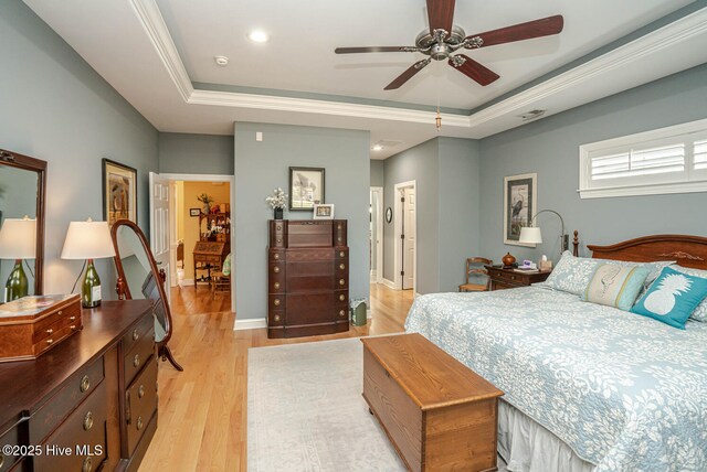 bedroom with baseboards, light wood-type flooring, a raised ceiling, and crown molding