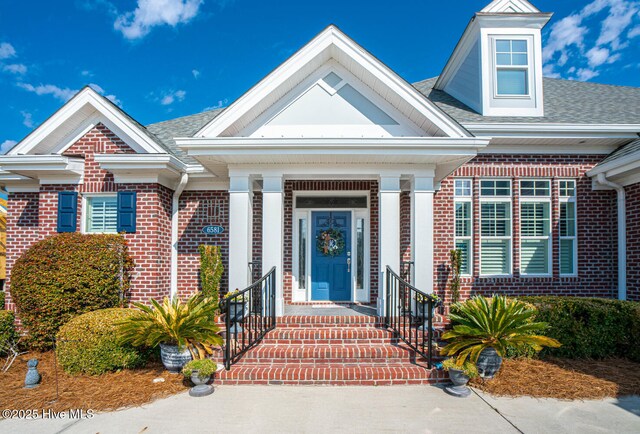 view of exterior entry with brick siding and a shingled roof